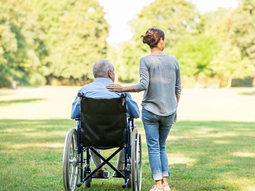 Eine Pflegerin spaziert im Park mit einem Senior im Rollstuhl
