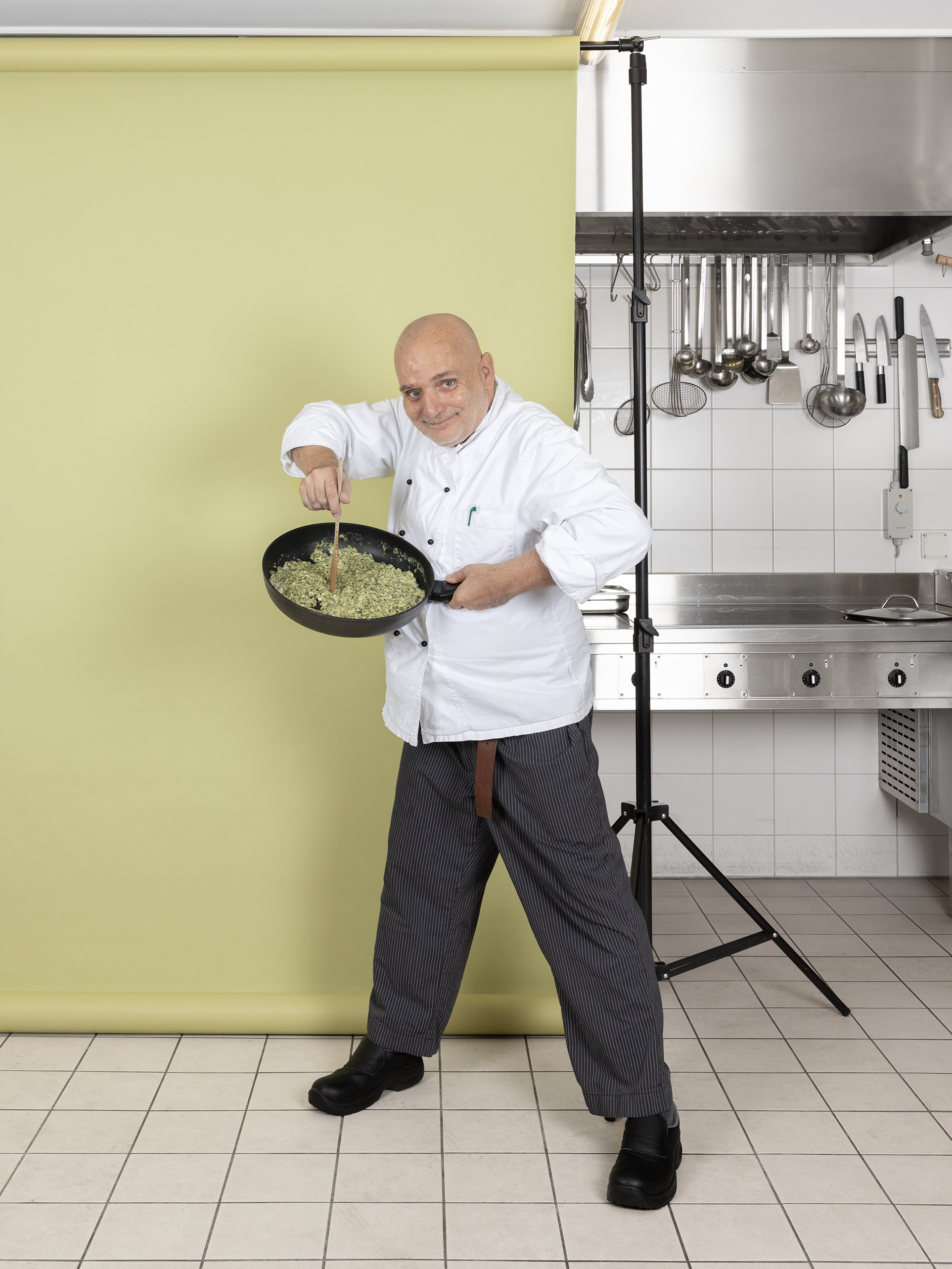Ein Foto aus dem Buch "Ohne Milch und Zucker". André Karlen steht vor einer hellgrünen Leinwand und hält eine Pfanne hoch.