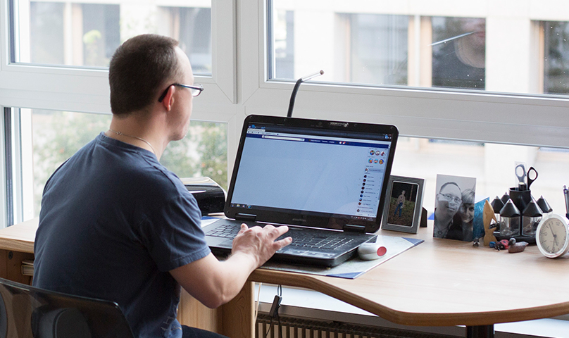 Eine Person sitzt mit einem Laptop an einem hellen Arbeitsplatz und arbeitet.