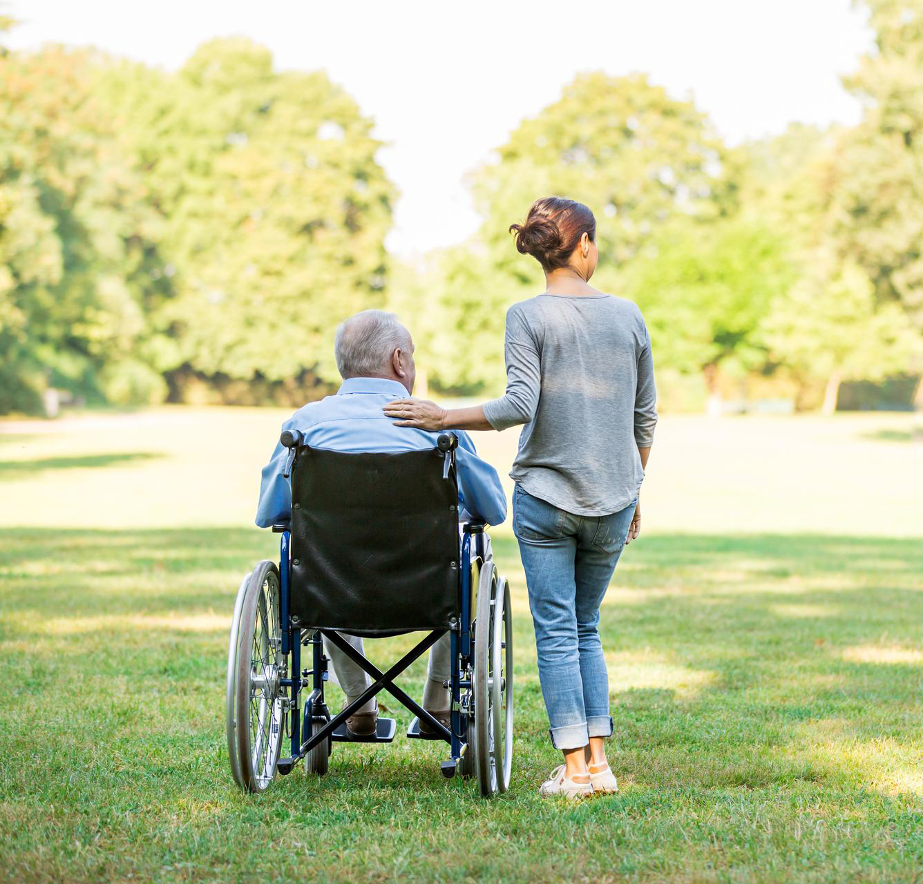 Eine Pflegerin spaziert im Park mit einem Senior im Rollstuhl