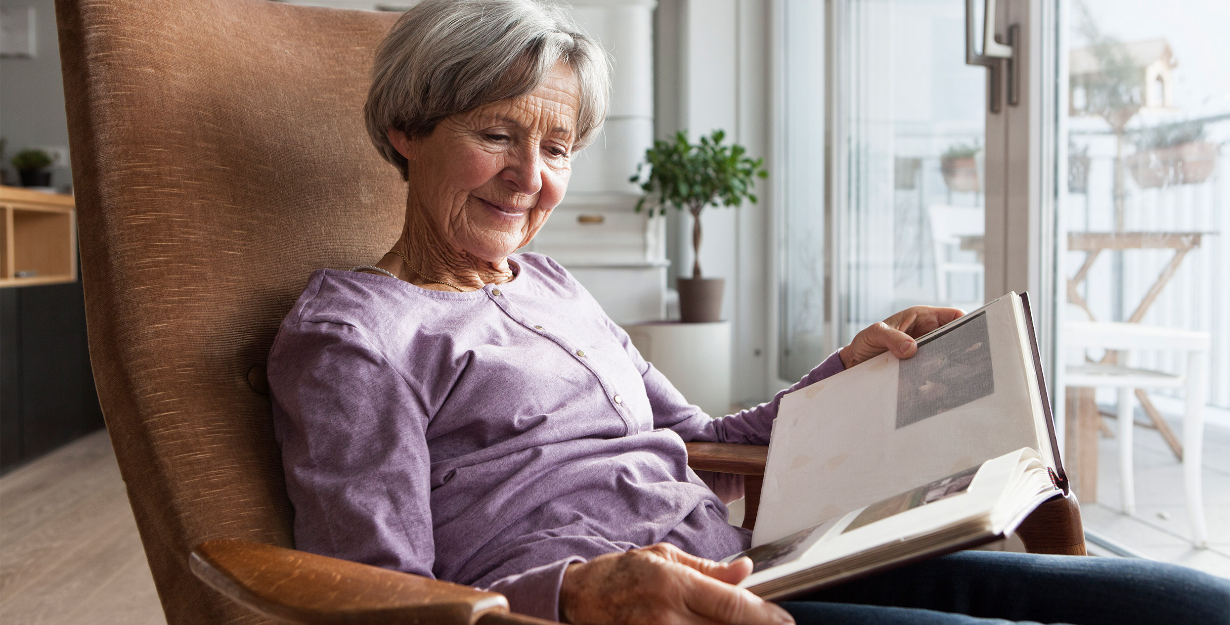 Seniorin im Sessel schaut sich ein Fotoalbum an