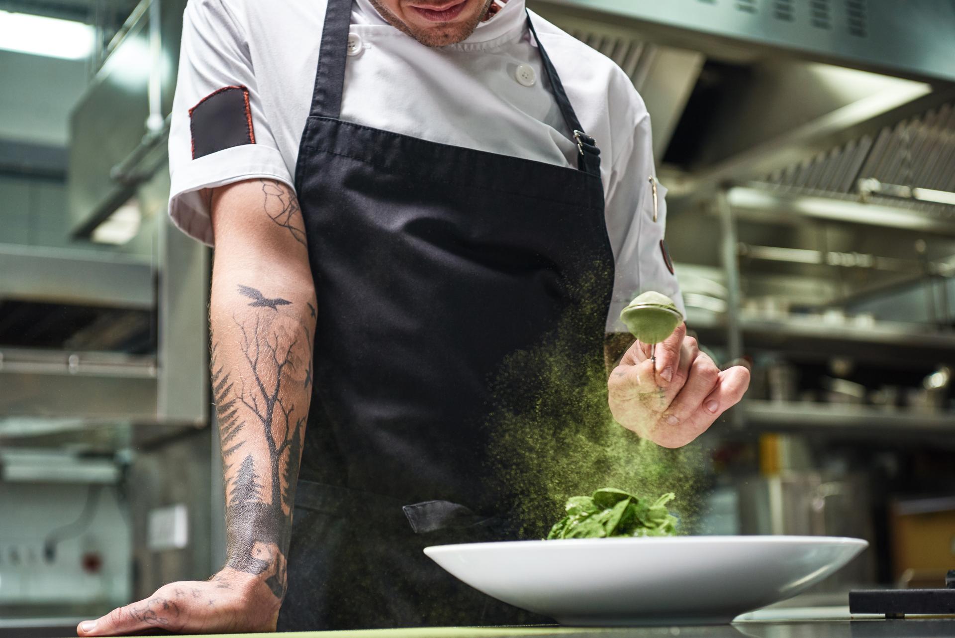 Eine Person streut mit einem kleinen Sieb Matcha-Pulver über ein Gericht