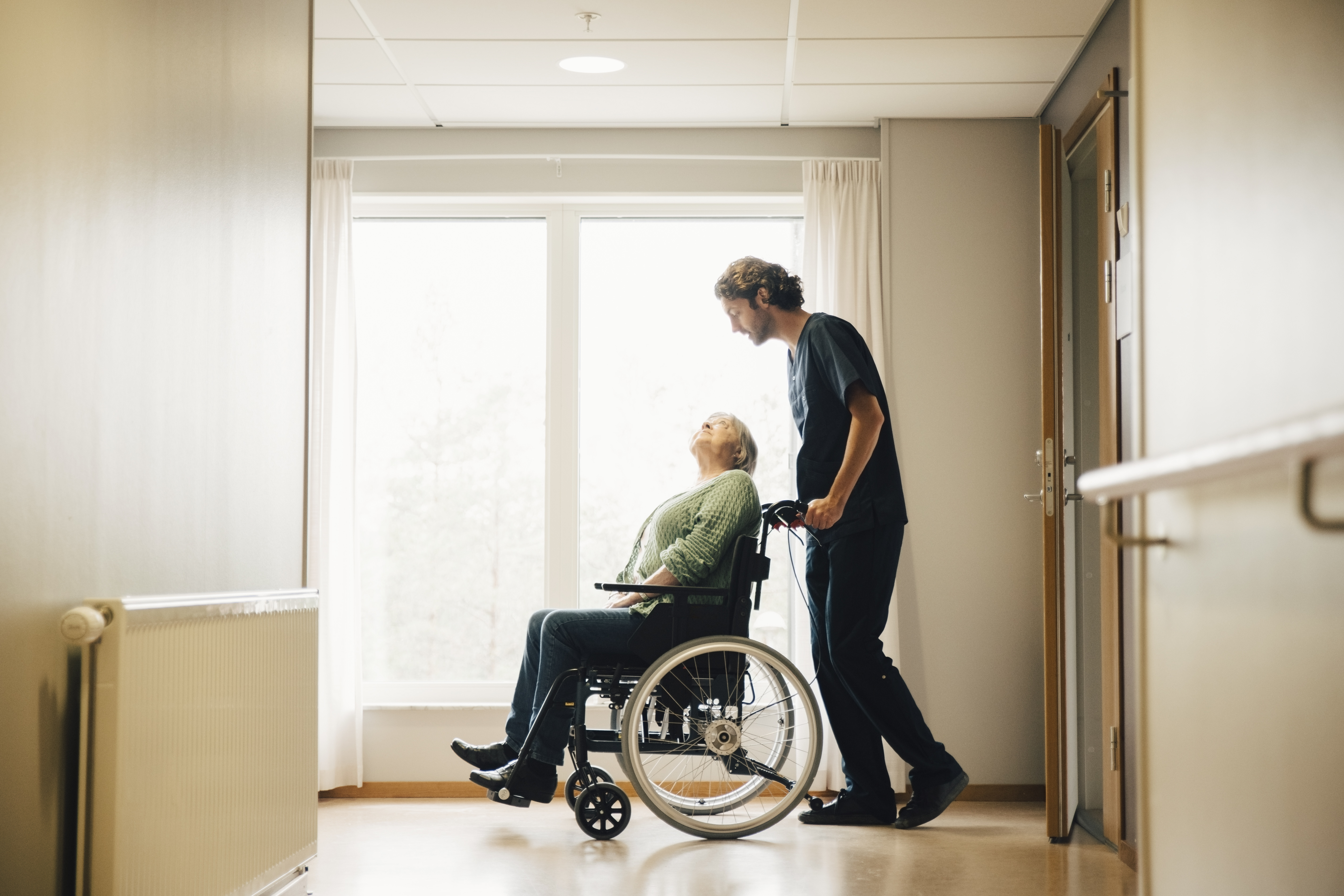 Pfleger schiebt Seniorin im Rollstuhl 
