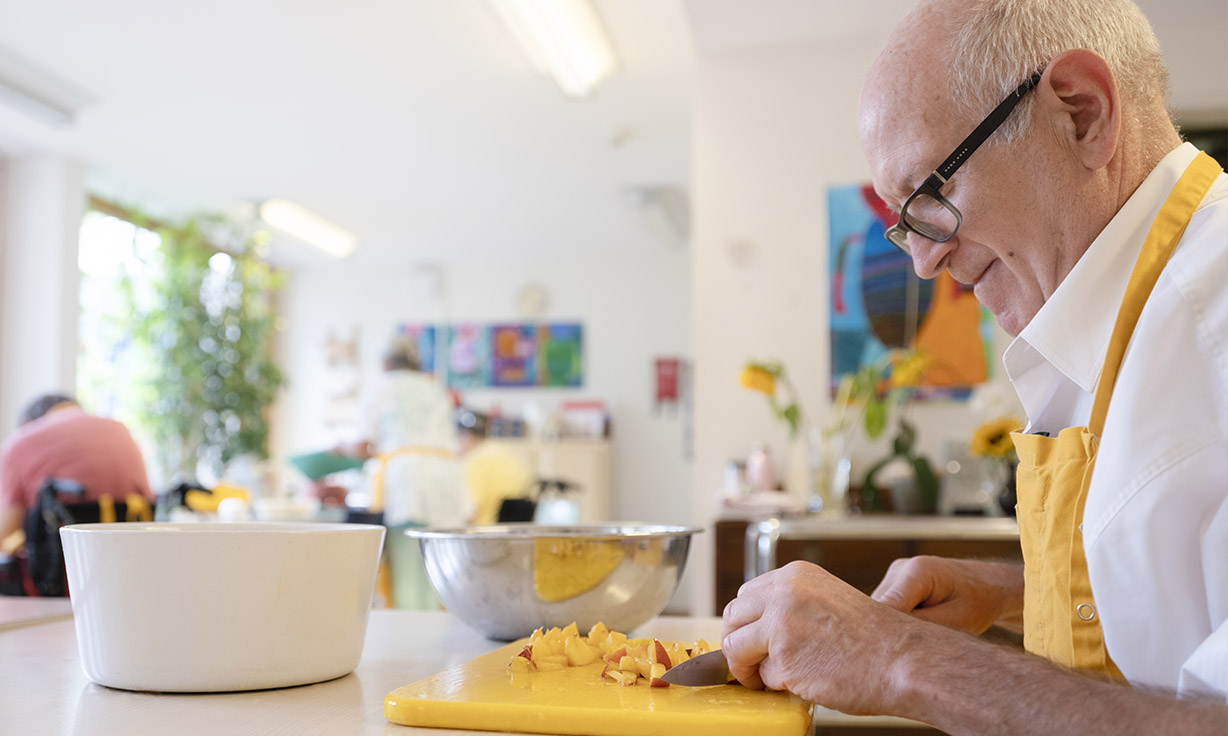 Ein Senior mit einer Kochschürze schneidet Früchte 