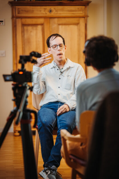 Mann vor Kamera im Interview mit Mann sitzend von hinten.