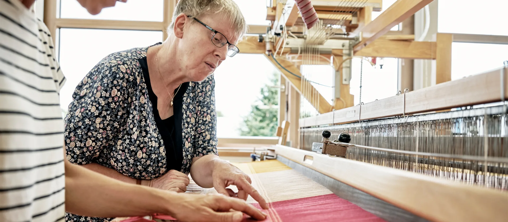 Zwei Personen betrachten die Textilarbeit auf einem Webstuhl
