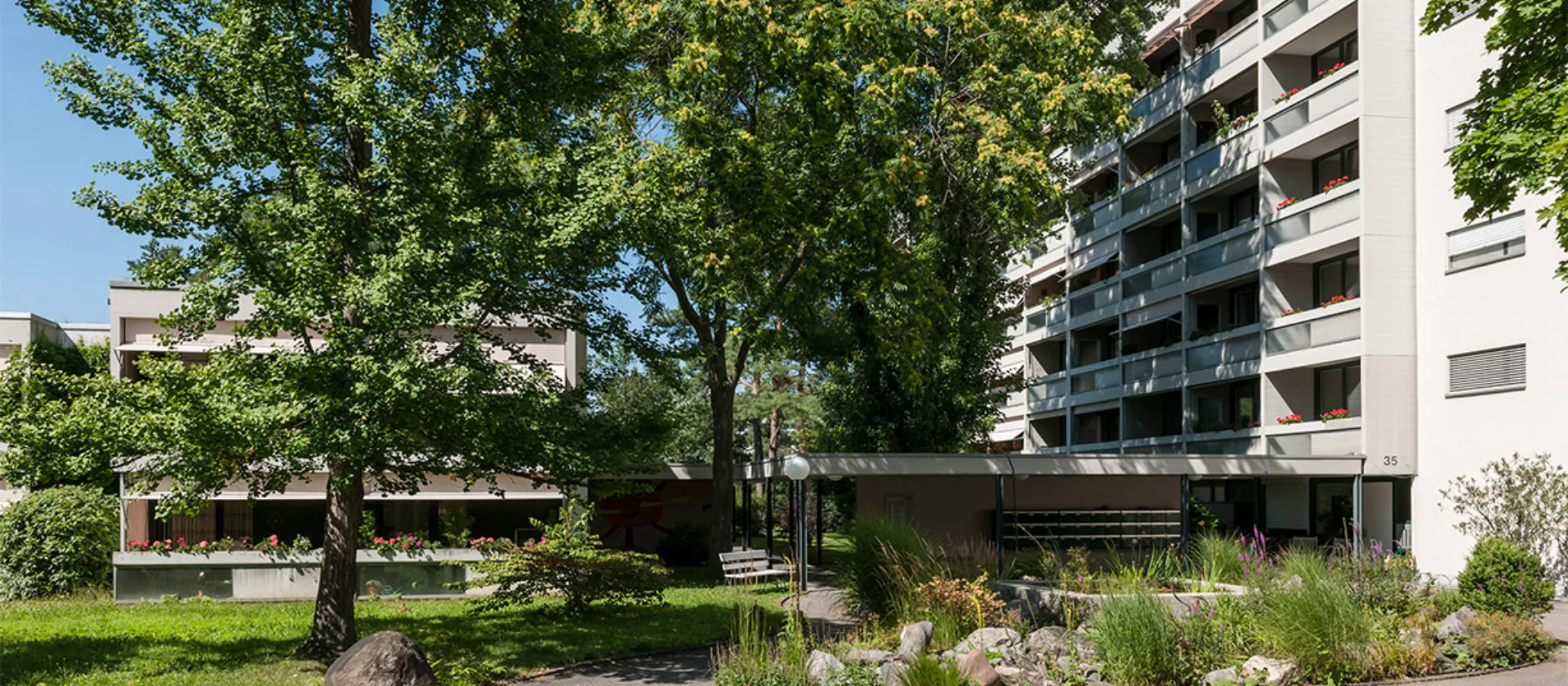 Ein Garten mit Bäumen zwischen den Gebäuden der Alterswohnungen Gellertfeld