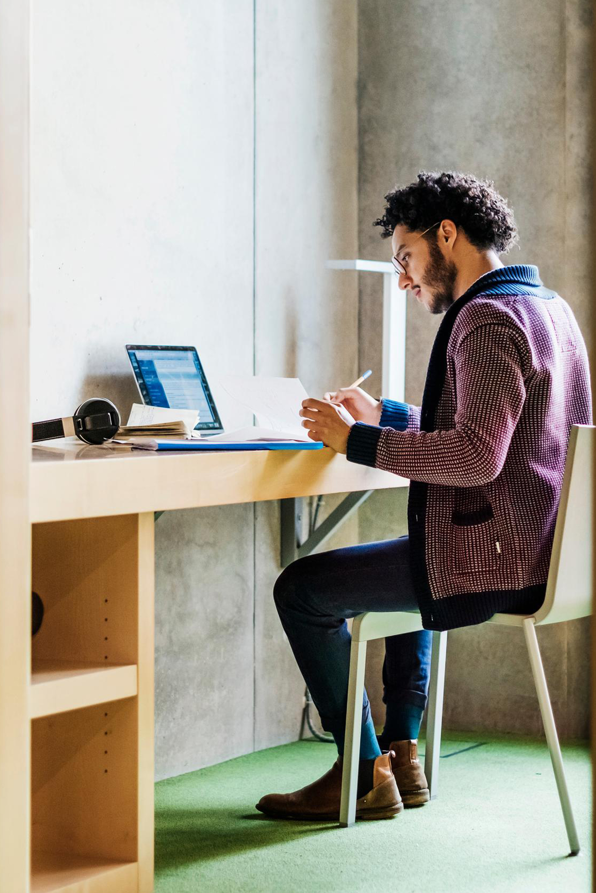 Eine Person sitzt am Tisch hält einen Stift in der Hand und arbeitet an einem Computer.