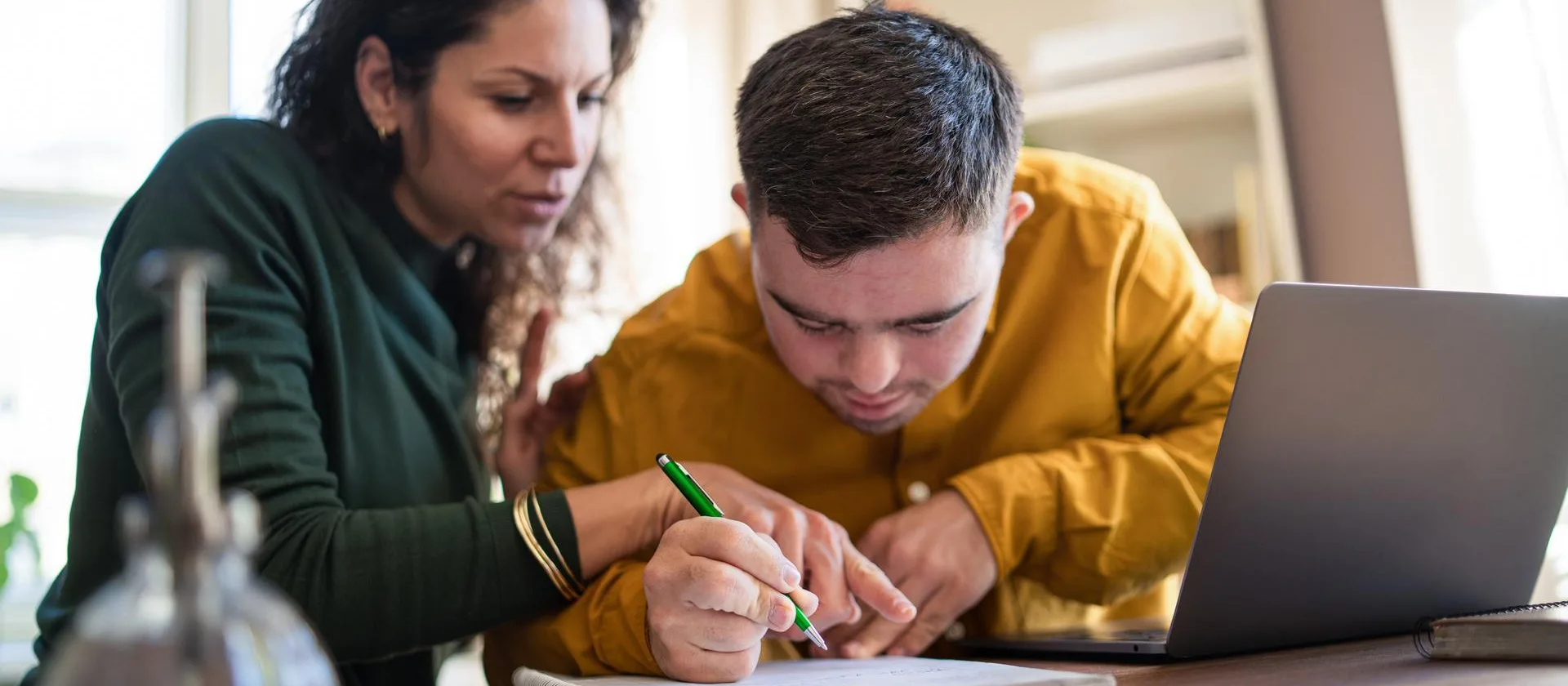 Junge Frau leistet einem Mann mit Einschränkung Unterstützung beim Lernen