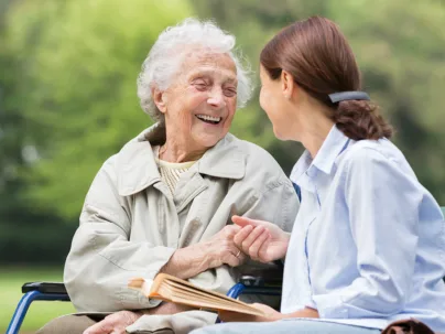 Seniorin und eine Junge Frau sitzen lachend auf einer Bank in der Natur