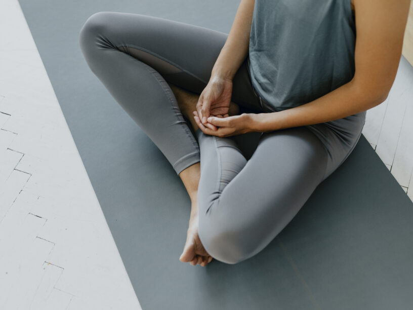 Person im Schneidersitz (Sukhasana) auf einer grauen Matte.