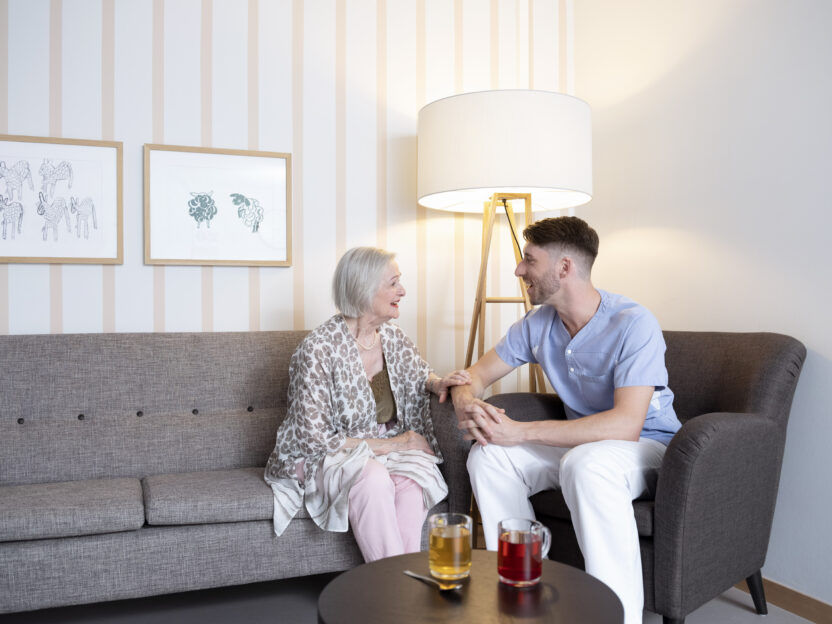 zufriedene Seniorin und Pfleger trinken gemeinsam Tee und sind im Austausch