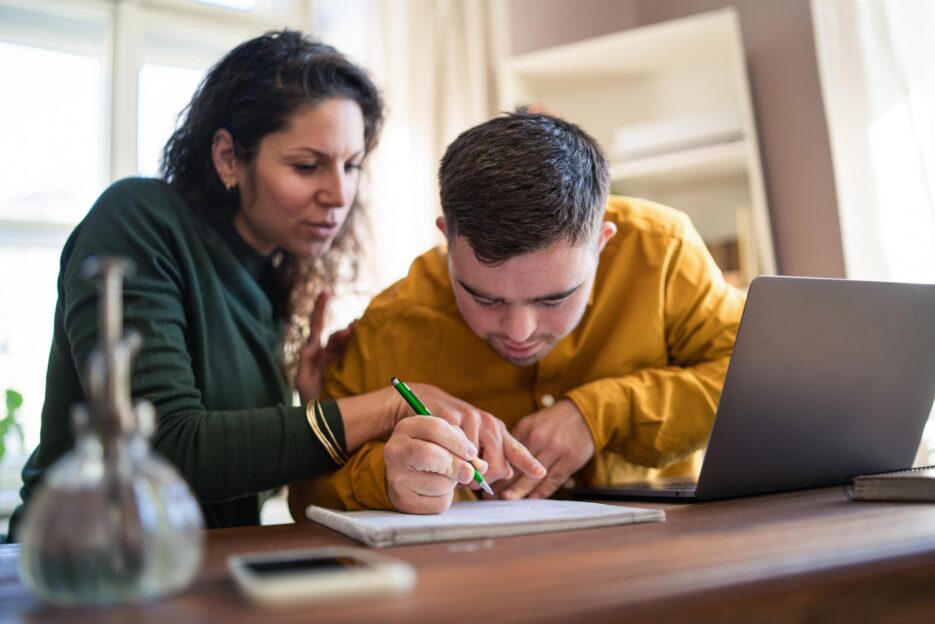Junge Frau leistet einem Mann mit Einschränkung Unterstützung beim Lernen
