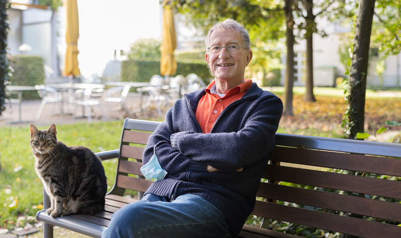 Rentner auf Bank im Park mit Katze neben an