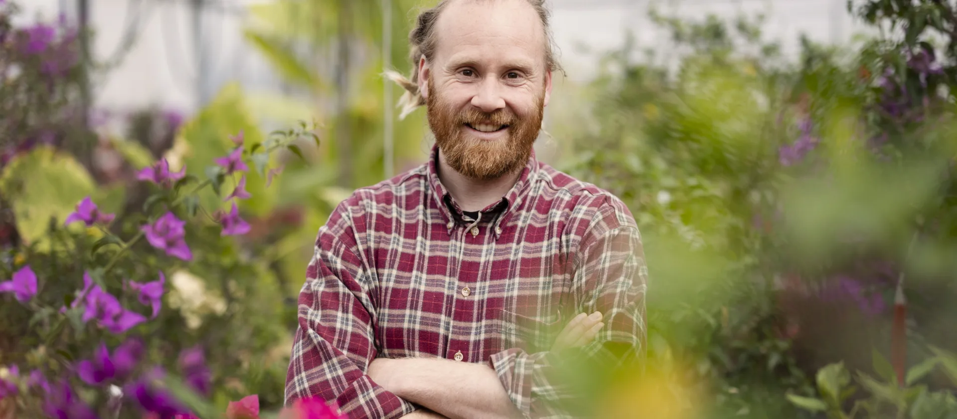 Ein Portraitfoto von David Brand, der in einem Gewächshaus steht und in die Kamera lächelt